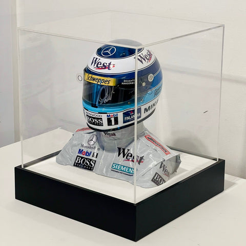 A clear acrylic display case with a black base holding a Mika Hakkinen 1/2 model helmet 